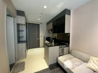 Modern compact kitchen with sleek black cabinets and cozy living area in a stylish apartment.