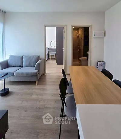 Modern open-plan living room with stylish furniture and wooden flooring, leading to a bedroom and bathroom.