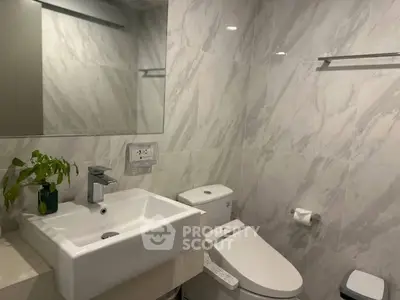 Modern bathroom with sleek fixtures and marble walls, featuring a stylish sink and toilet.