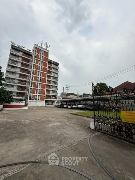 Modern apartment building with spacious parking area and secure entrance gate.