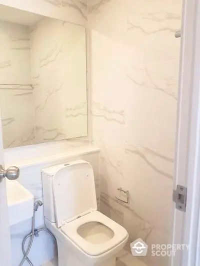 Elegant bathroom with marble walls and modern fixtures, featuring a sleek toilet and a large mirror, perfect for a contemporary home.