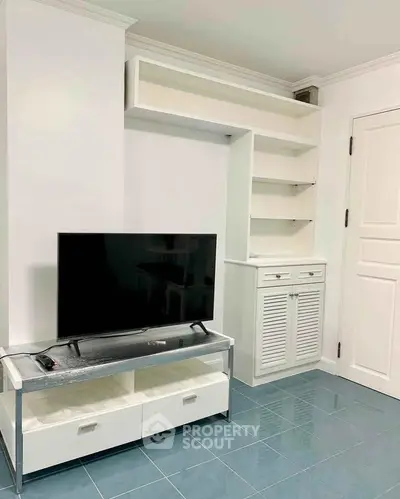 Modern living room with sleek TV stand and built-in shelving, featuring glossy blue tile flooring.