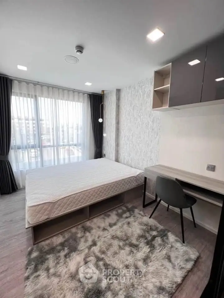 Modern bedroom with large window, stylish decor, and cozy rug in a contemporary apartment.