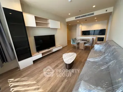 Modern living room with sleek furniture and open kitchen layout, featuring a large TV and stylish decor.