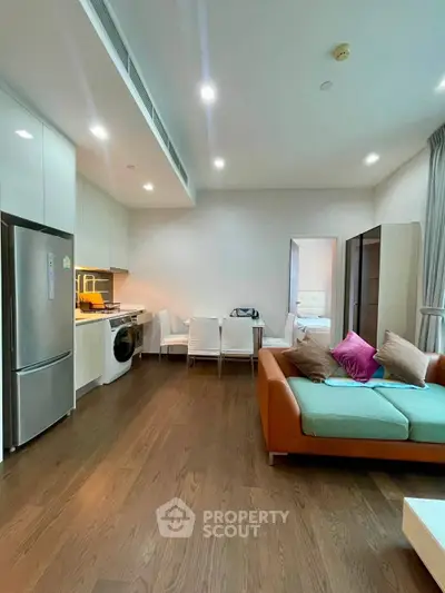 Modern open-layout living room with kitchen, featuring sleek appliances and stylish furniture.