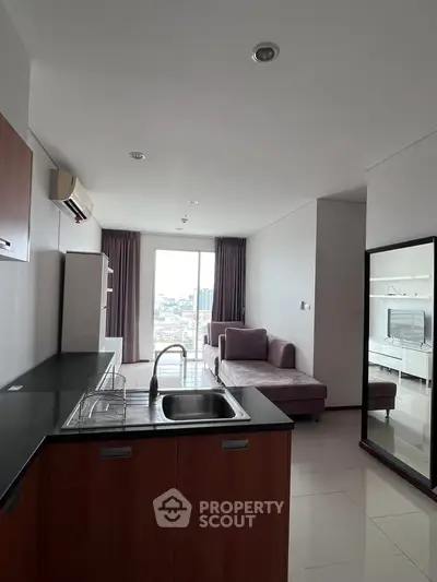Modern open-plan living room with sleek kitchen and city view, featuring stylish furniture and ample natural light.
