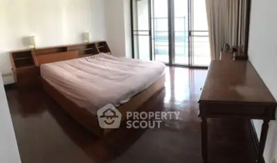 Spacious bedroom with wooden flooring and large windows leading to a balcony.