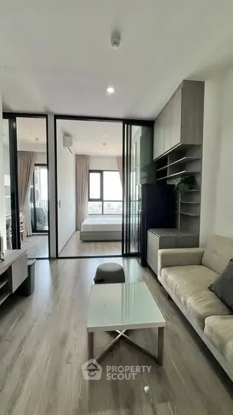 Modern apartment interior with open living room and bedroom, featuring sleek design and natural light.