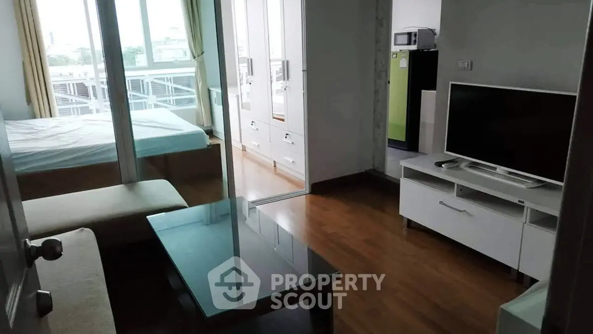Modern studio apartment with glass coffee table and TV, featuring a cozy bedroom and large windows.