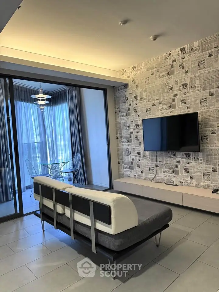 Modern living room with stylish newspaper wallpaper and sleek furniture, opening to a bright balcony area.