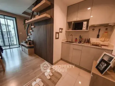 Modern open-plan living room with stylish kitchen and staircase, featuring sleek cabinetry and natural light.