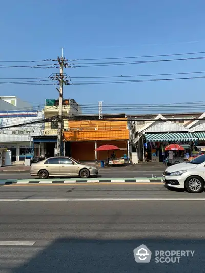 Street view of commercial buildings with parked cars and clear blue sky.