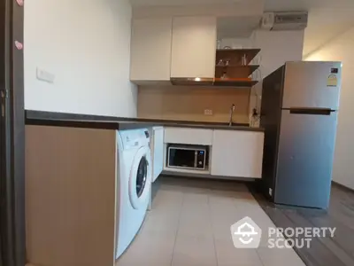 Modern kitchen with washing machine, microwave, and fridge in sleek apartment