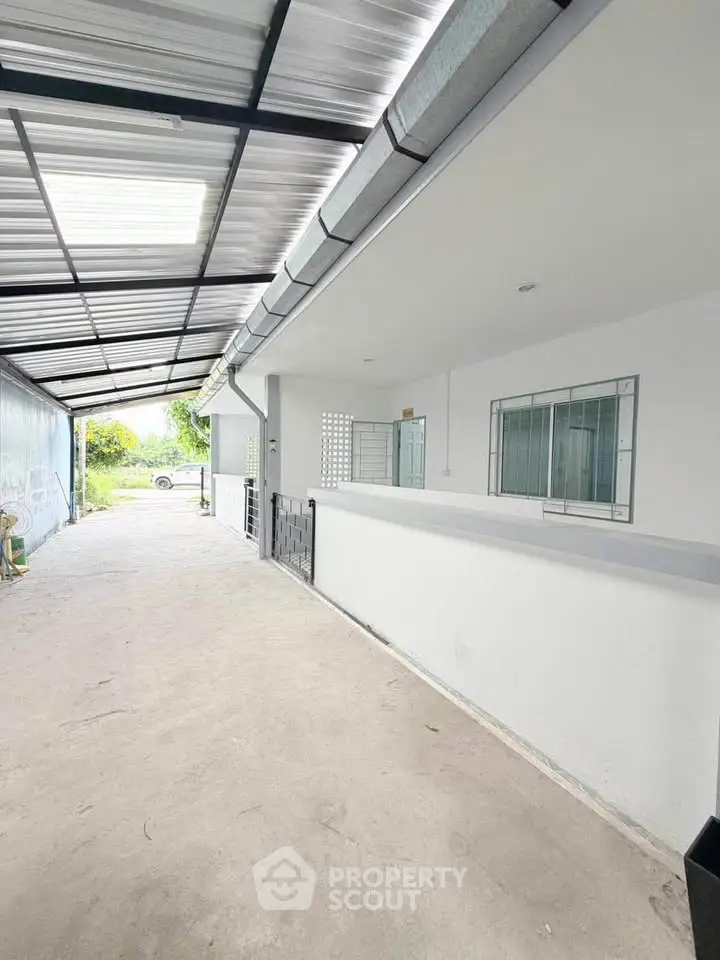 Spacious covered outdoor area with modern white walls and large window, perfect for versatile use.
