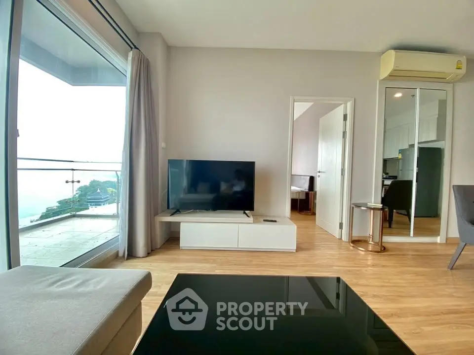 Modern living room with large window and balcony view, featuring sleek furniture and wooden flooring.