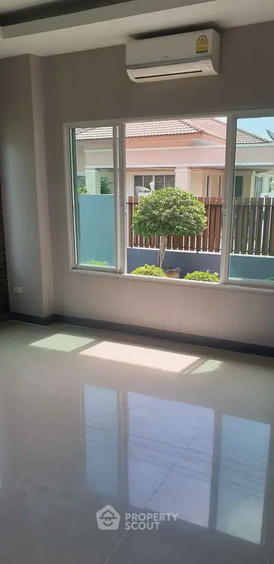 Bright living room with large windows and garden view, featuring sleek tiled flooring and air conditioning.