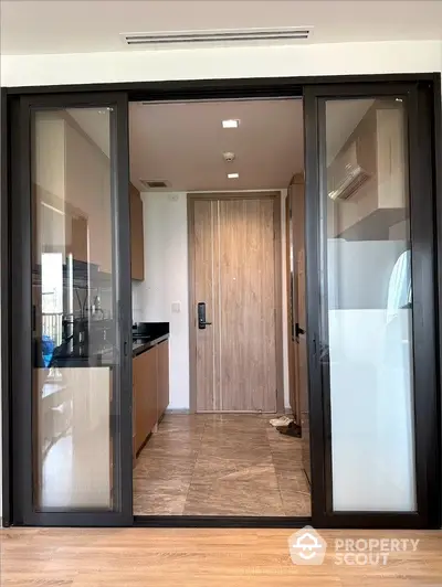 Sleek modern kitchen with black countertops and wooden accents, leading to a welcoming entryway with elegant flooring and a secure door.