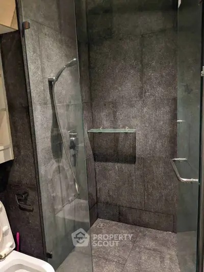 Modern bathroom with sleek glass shower enclosure and dark textured tiles.