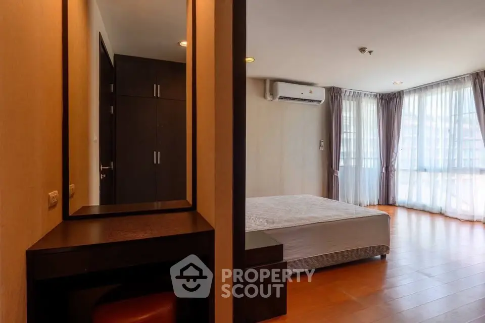 Spacious bedroom with large windows and modern furnishings in a well-lit apartment.