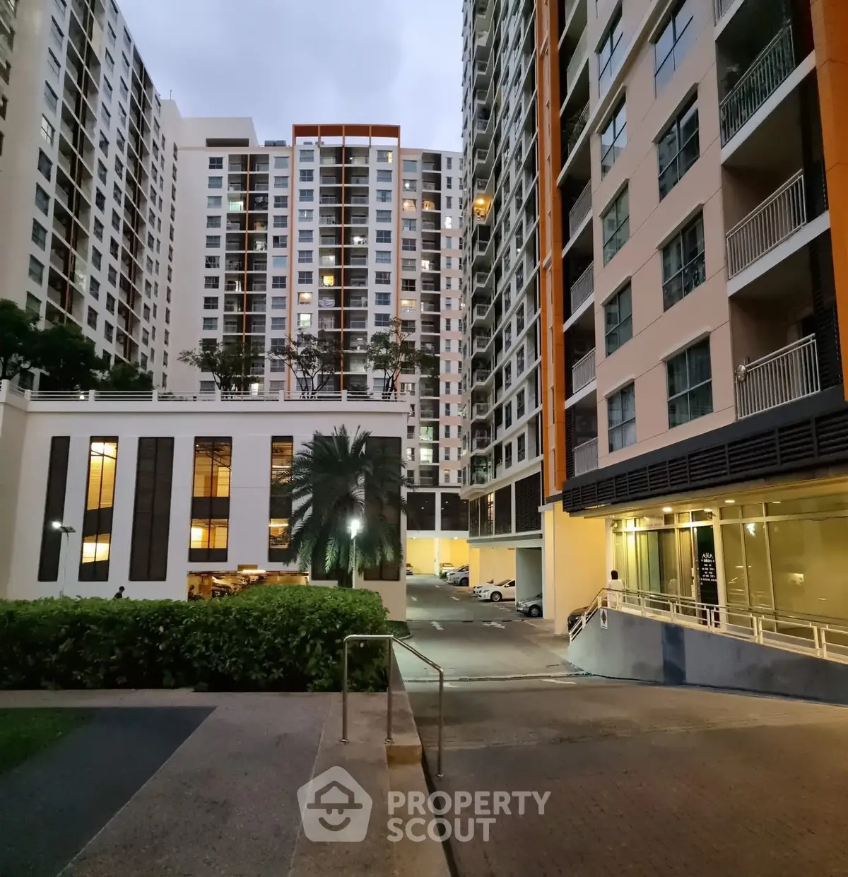 Modern high-rise residential building with well-lit entrance and lush greenery.