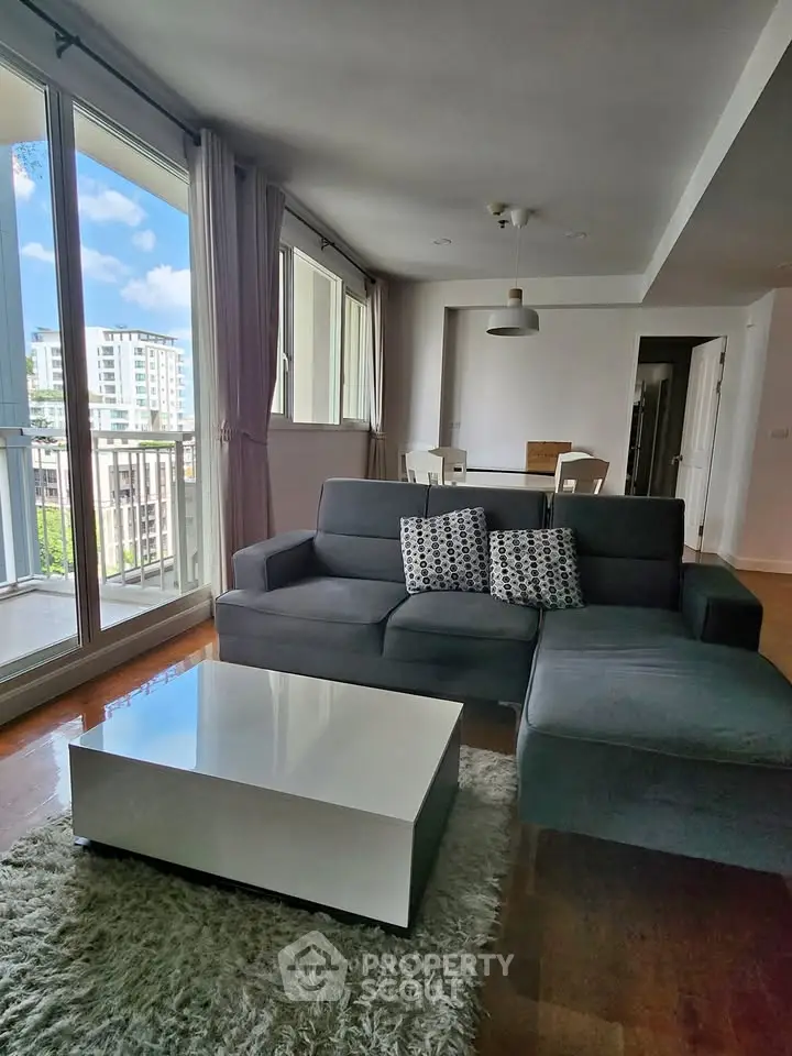 Spacious modern living room with large windows and city view, featuring a stylish sofa and sleek coffee table.