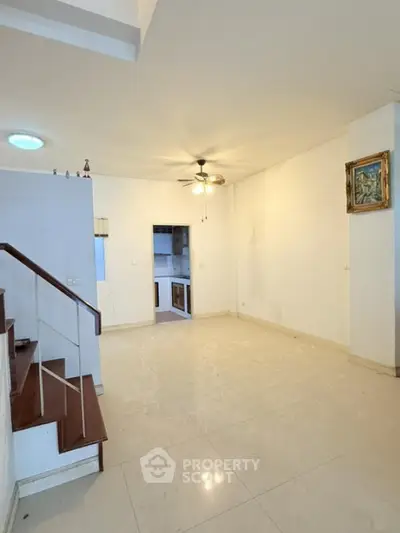 Spacious living room with modern ceiling fan and staircase leading to upper level.