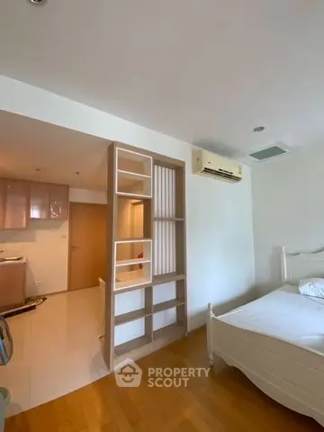 Spacious bedroom with modern design and air conditioning, featuring wooden flooring and open shelving.