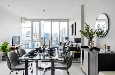 Modern living room with dining area and city view, featuring sleek furniture and large windows.