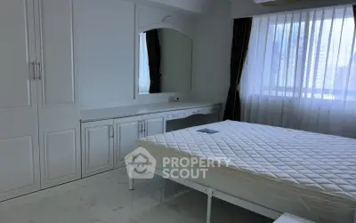 Spacious bedroom with elegant white furnishings and large window offering natural light.