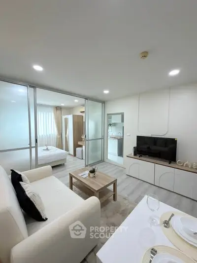 Modern open-plan living room with sleek furniture and a view into a cozy bedroom.