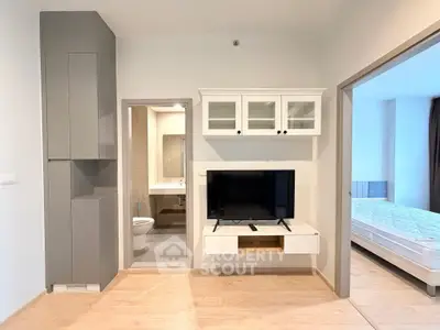 Modern apartment interior with open living area, TV unit, and view into bedroom and bathroom.