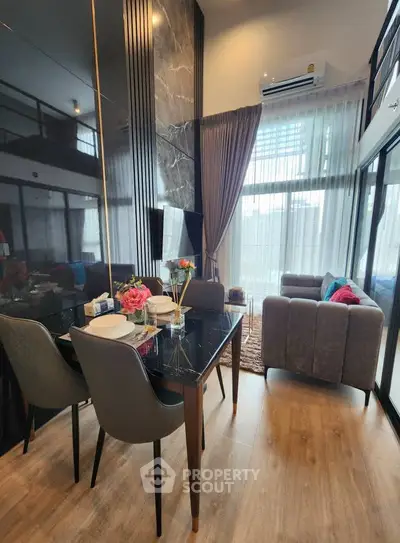 Modern living room with dining area, high ceiling, and large windows for natural light.