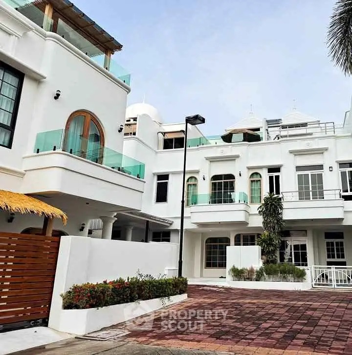 Stunning white modern townhouse with glass balconies and lush greenery.
