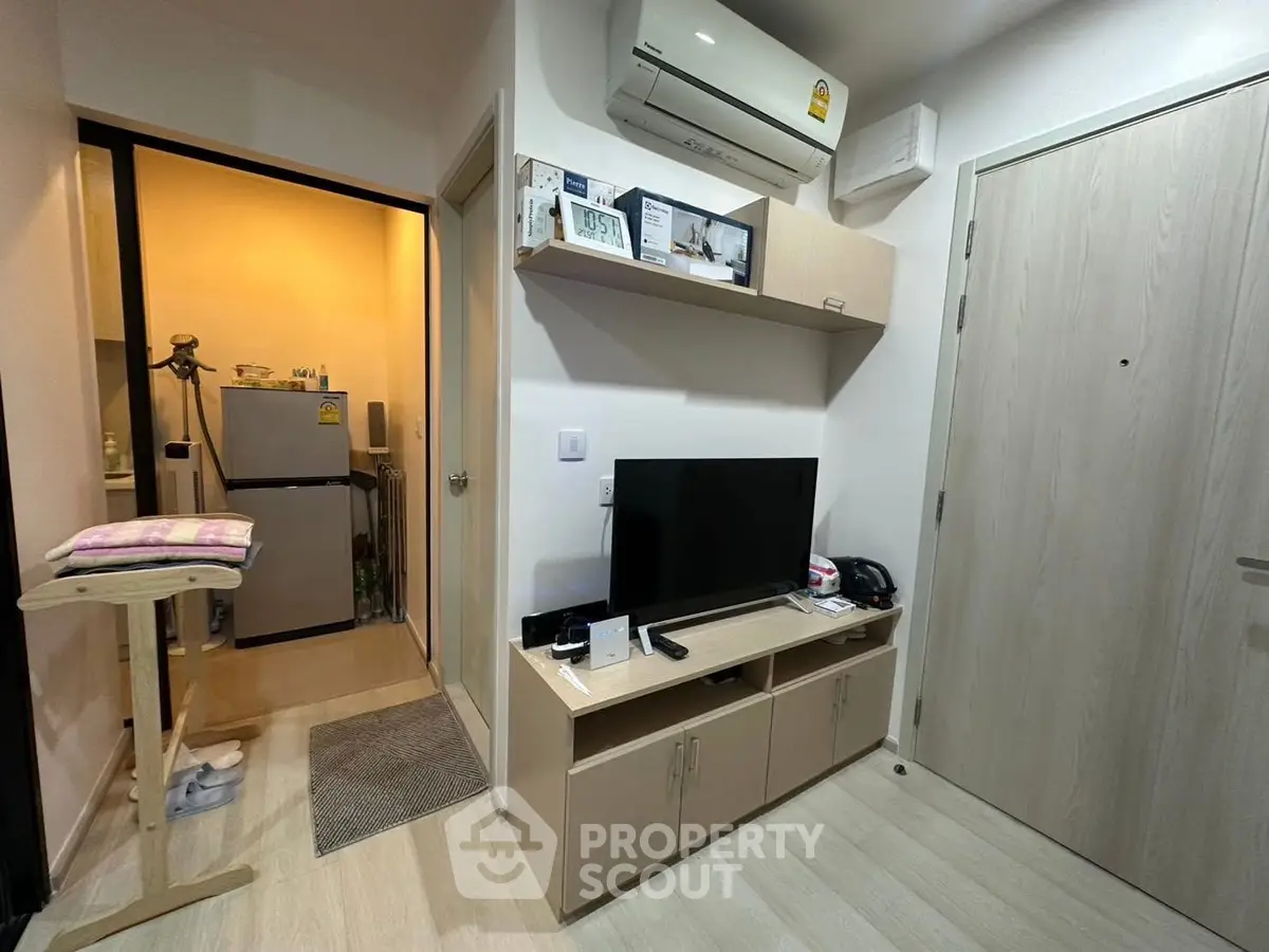 Cozy apartment interior with modern TV setup and compact kitchen area.