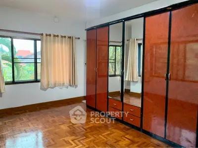 Spacious bedroom with elegant wooden flooring and large mirrored wardrobe.
