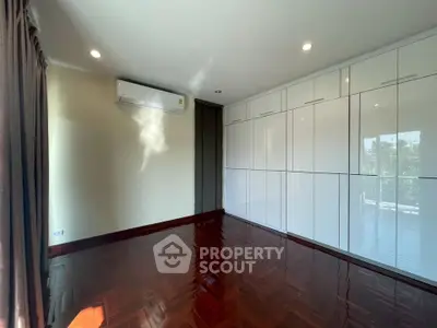 Spacious bedroom with glossy wooden floors and built-in wardrobes, featuring ample natural light.