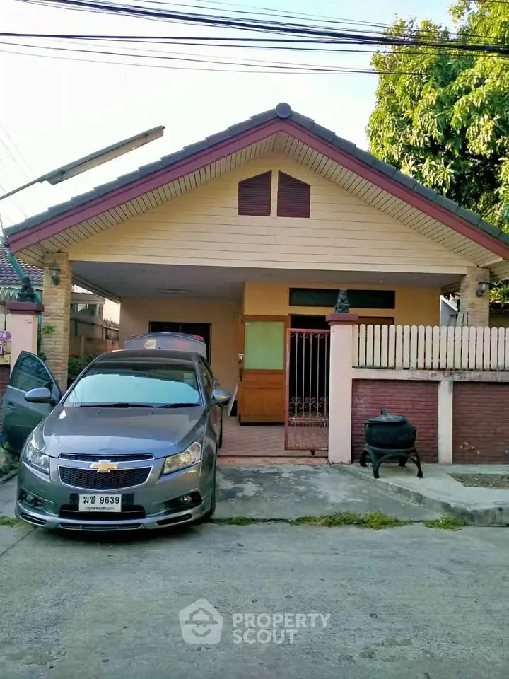 Charming single-story house with driveway and car parked in front, featuring a cozy entrance and lush greenery.