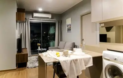 Modern open-layout living room with kitchen and city view, featuring cozy decor and washing machine.