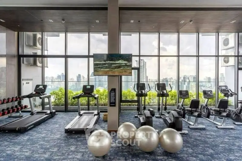 Modern gym with city view, featuring treadmills, ellipticals, and exercise balls in a high-rise building.