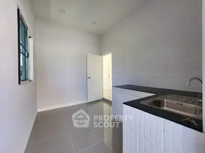 Modern minimalist kitchen with sleek white cabinetry and black countertop, featuring a stainless steel sink.