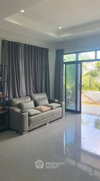 Spacious living room with modern sofa and large windows opening to a lush garden view.