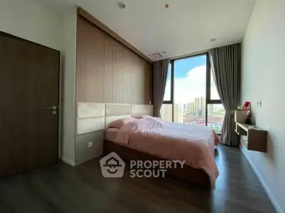Modern bedroom with large window offering city view, featuring elegant decor and wooden flooring.