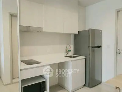 Modern compact kitchen with sleek cabinetry and stainless steel fridge in a minimalist apartment.