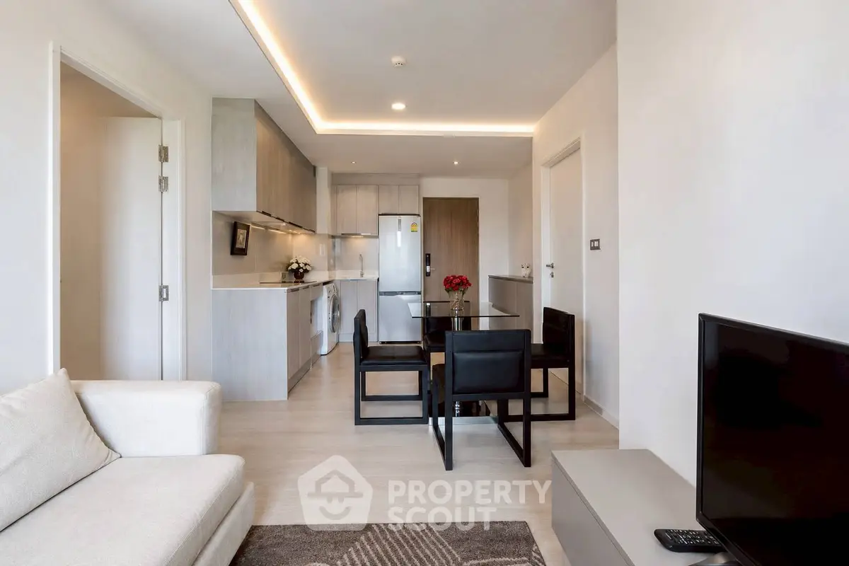 Modern open-plan living room with sleek kitchen and dining area, featuring contemporary furniture and neutral tones.