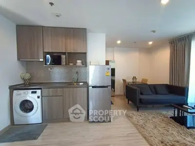 Modern open-plan living room with kitchen, featuring washing machine and fridge, stylish sofa, and dining area.