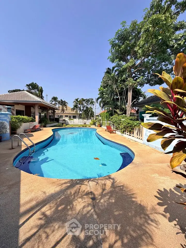 Stunning outdoor pool area with lush greenery and clear blue skies, perfect for relaxation and leisure.