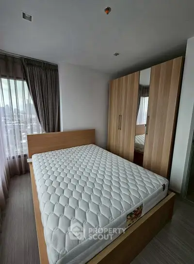 Modern bedroom with large window and wooden wardrobe, offering city views.