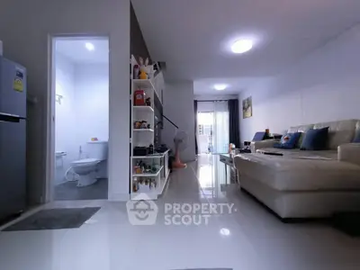 Modern living room with sleek white tiles and cozy beige sofa, open to a compact bathroom.