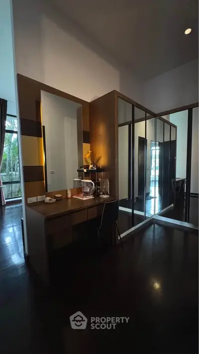 Elegant bedroom with mirrored wardrobe and vanity, featuring dark wood flooring and garden view.
