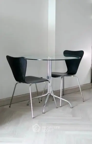 Modern minimalist dining area with glass table and sleek black chairs.